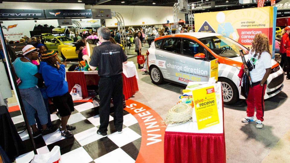 Black and white checker vinyl floor graphic in busy tradeshow booth with a wrapped vehicle and many people