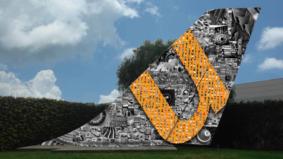 Airplane tailfin wrap with black and white mechanical images and Orange U on grass outside.