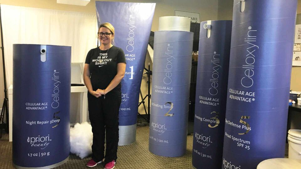 Trade show display featuring large vinyl wrapped Apriori Beauty products with blue and white colorway
