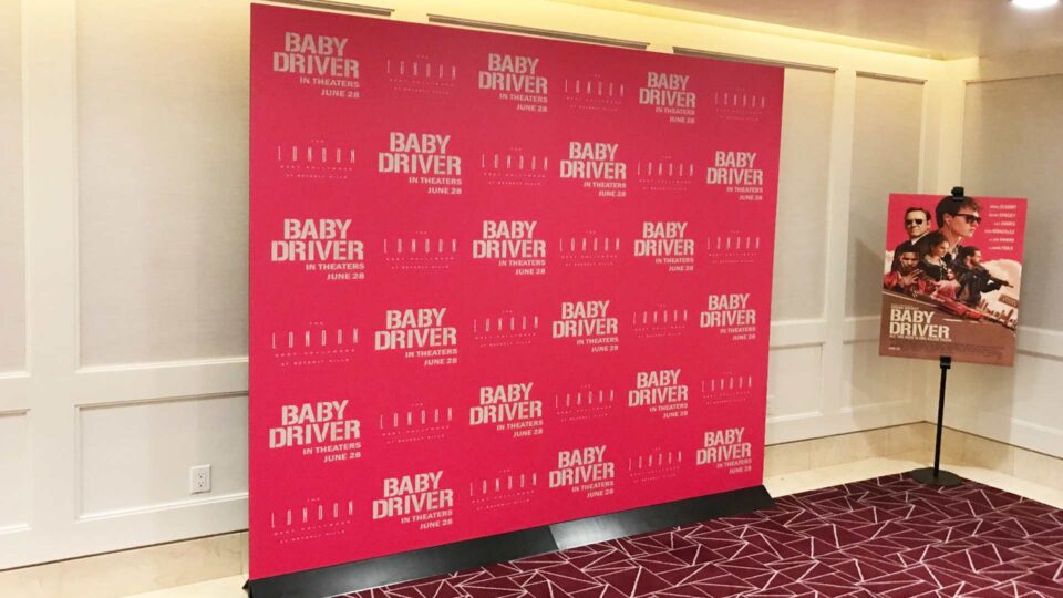 Pink step and repeat wall with white Baby Driver Movie logo in a room with a Baby Driver poster