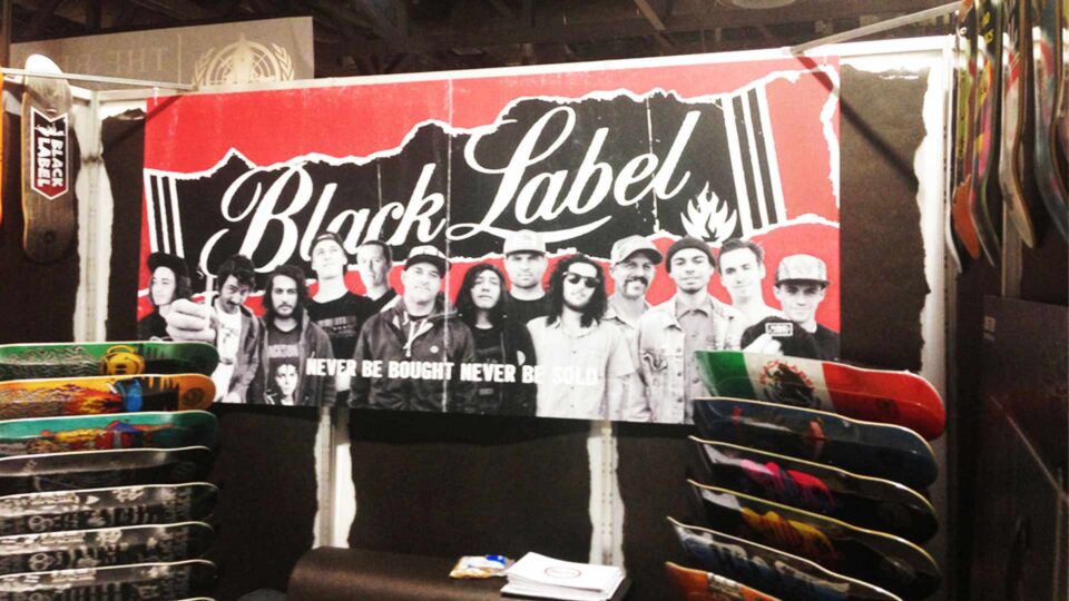 Red, black and white Black Label banner with team of skateboarders in trade show booth with colorful skateboards displayed.