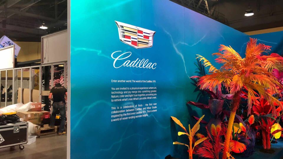 Trade show booth wall with blue water background, colorful sea plants and Cadillac log with text in white.