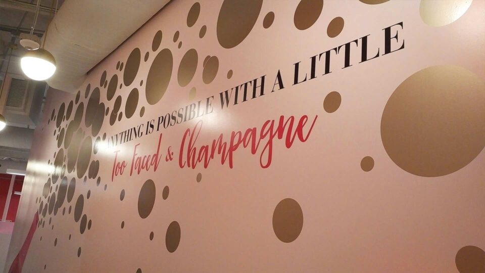 Pink wall with gold die cut decal bubbles and text for Too Faced Cosmetics