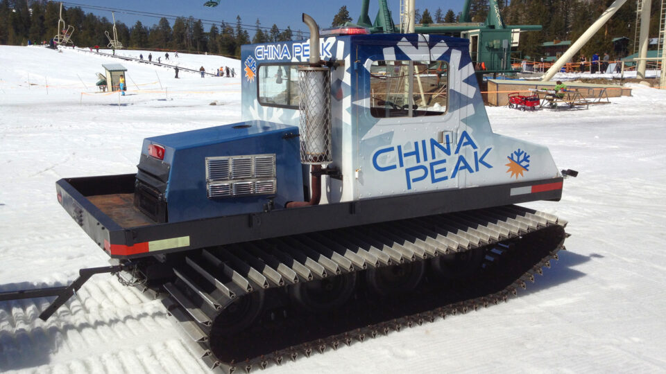 Snow groomer vinyl wrap that says CHINA Peak with logos in blue, white and yellow, parked in snow at ski resort