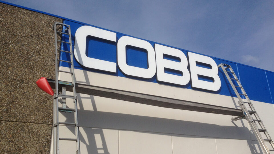 Large white lettered sign that says COBB in white with blue background on top of building. Laddeds and scaffolding