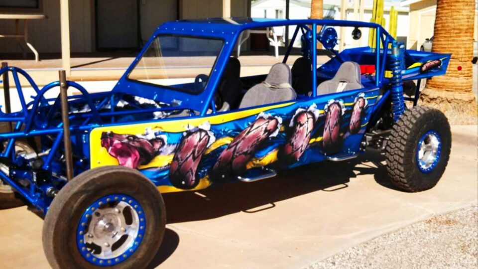 Blue dune buggy wrap with coiled boa snake on side with blue and yellow background parked outside in desert