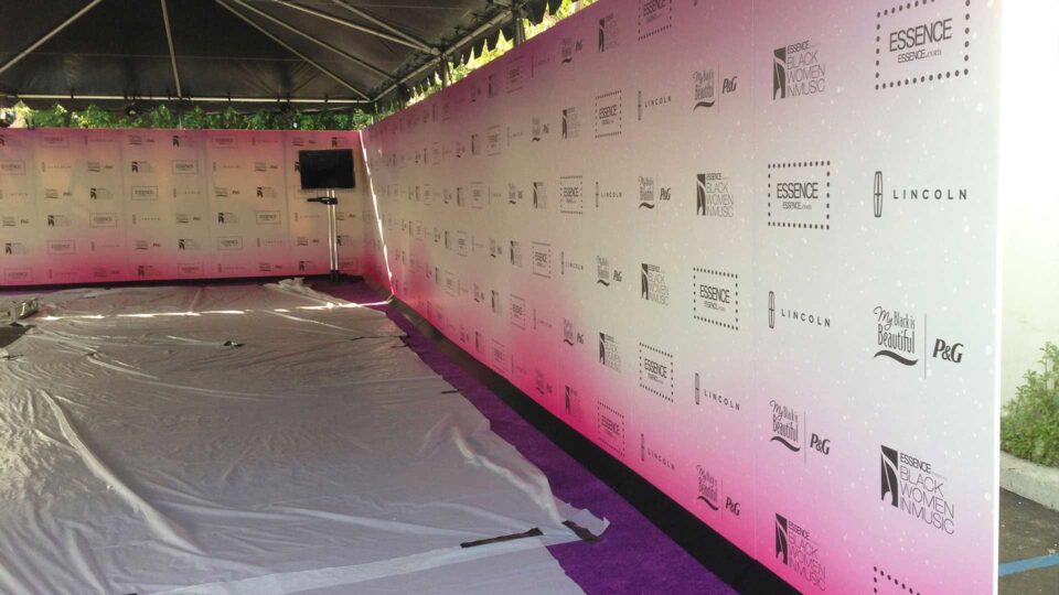 White & pink media wall with Essence and other logos in black on purple carpet for special event
