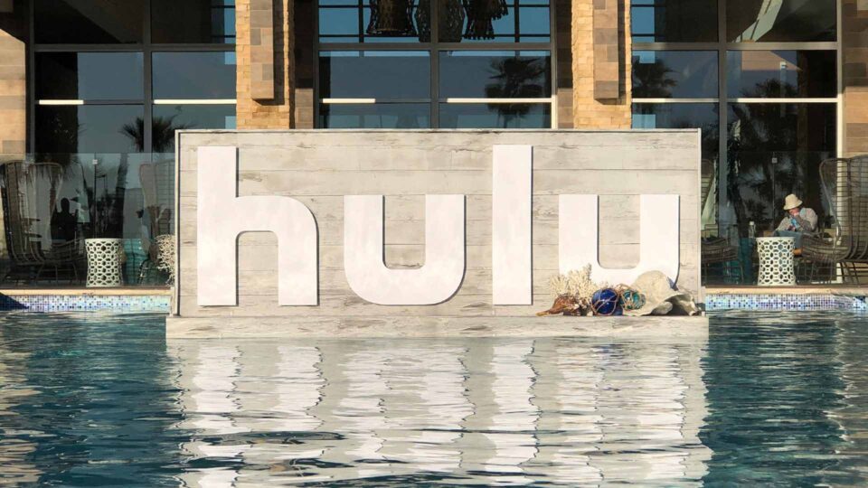 Wood foamboard sign with HULU in white floating in pool at sales meeting