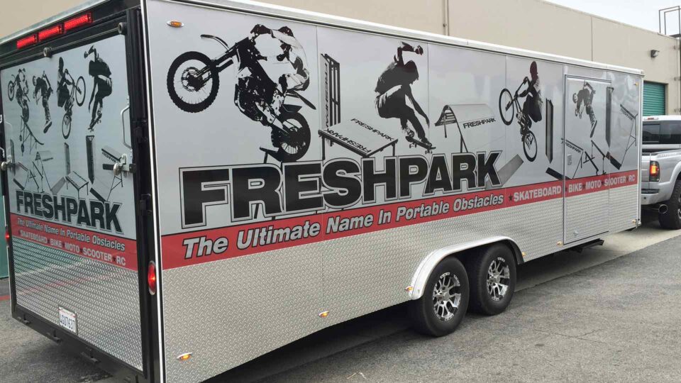 Gray, black and red Freshpark Logo on enclosed trailer featuring skateboard and moto riders and ramps