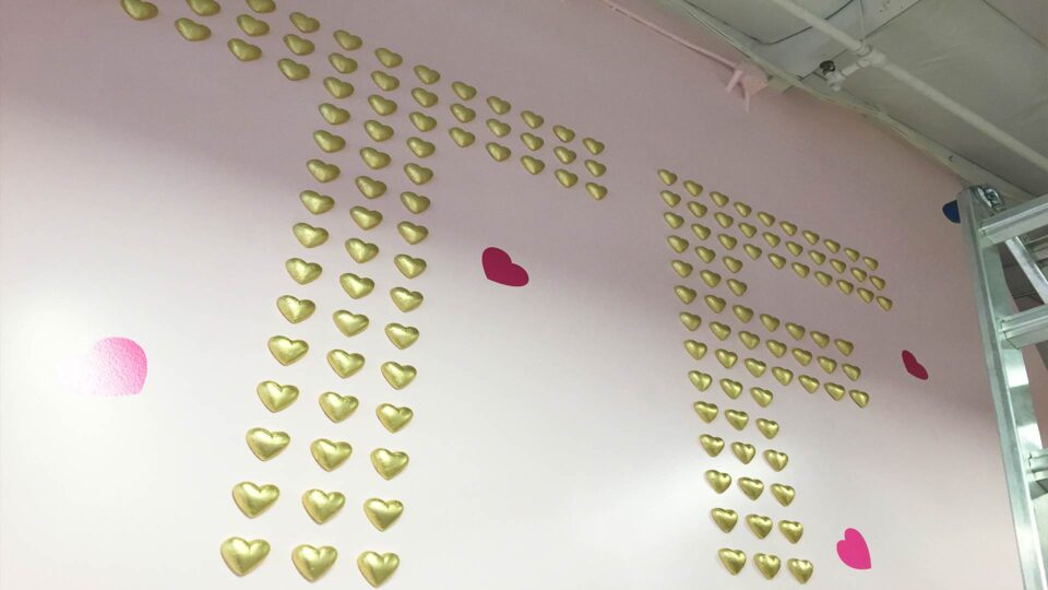 pink wall with gold raised hearts in the shape of T and F for Too Faced Cosmetics