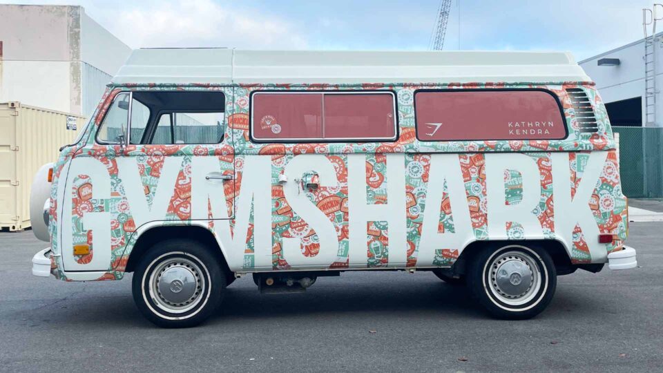 Full VW van wrap that has colorful background images and GYMSHARK large white lettering