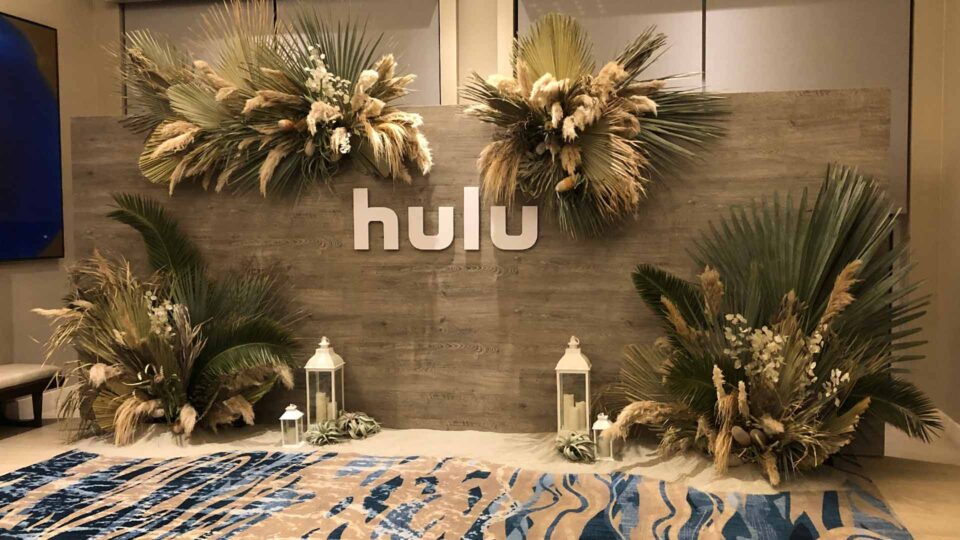 wood wall with HULU router cut letters in white and palm leaves and floral for sales meeting