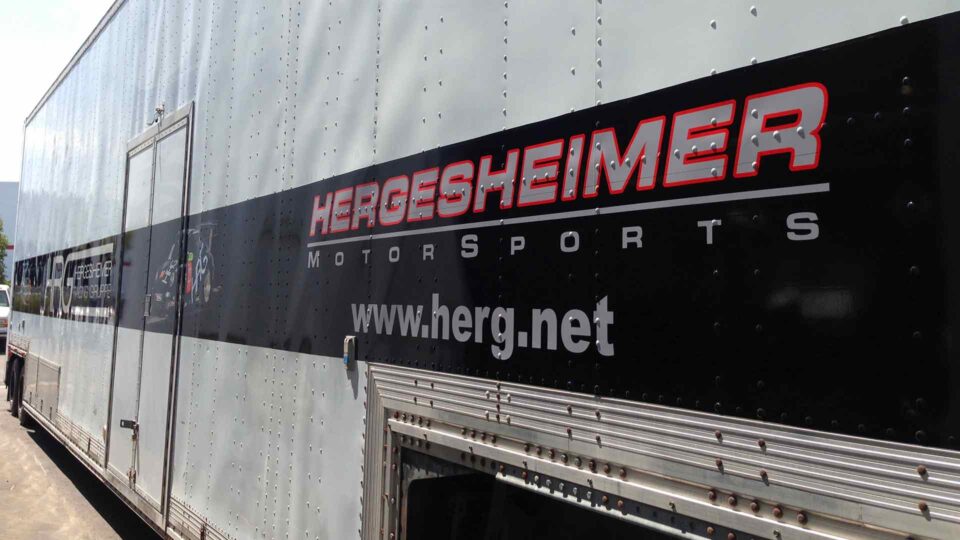 Silver semi trailer with black stripe partial wrap with Hergesheimer Motosports logo and brands