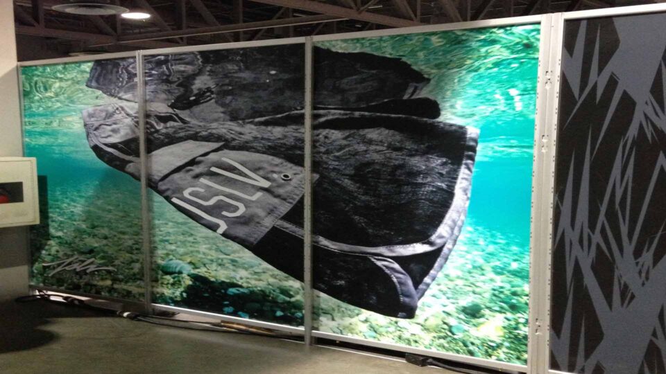 3 panel tradeshow wall graphics showing black JSLV board shorts under water in the ocean