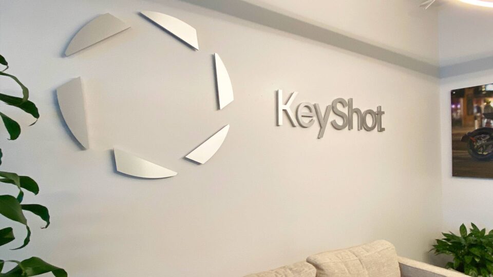 Silver Keyshot logo and name router cut sign on white lobby wall.