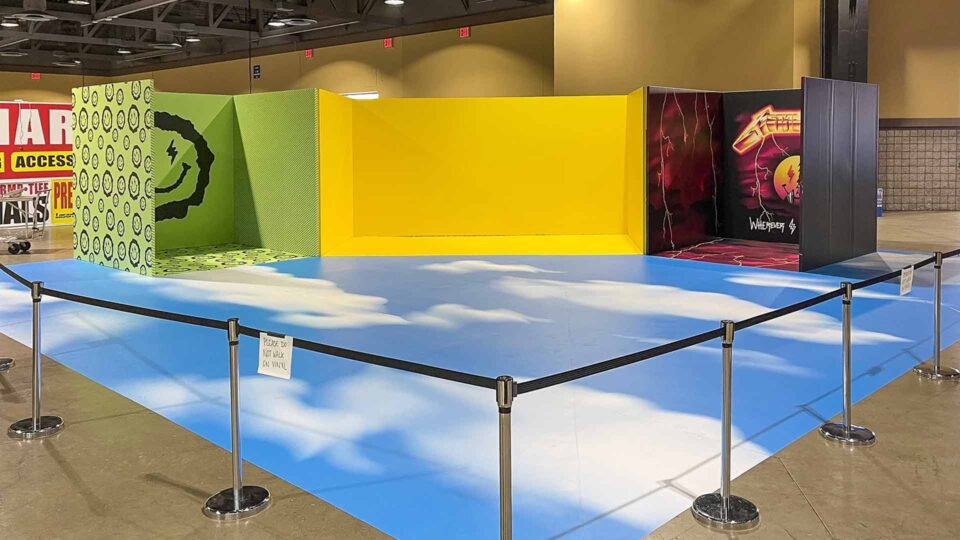 Blue sky with clouds vinyl trade show booth floor graphic with green, yellow and red vinyl booth walls
