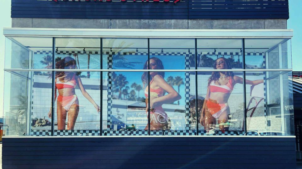 3 banners of model in pink toned bikini hanging in retail store window for L Space Swim.