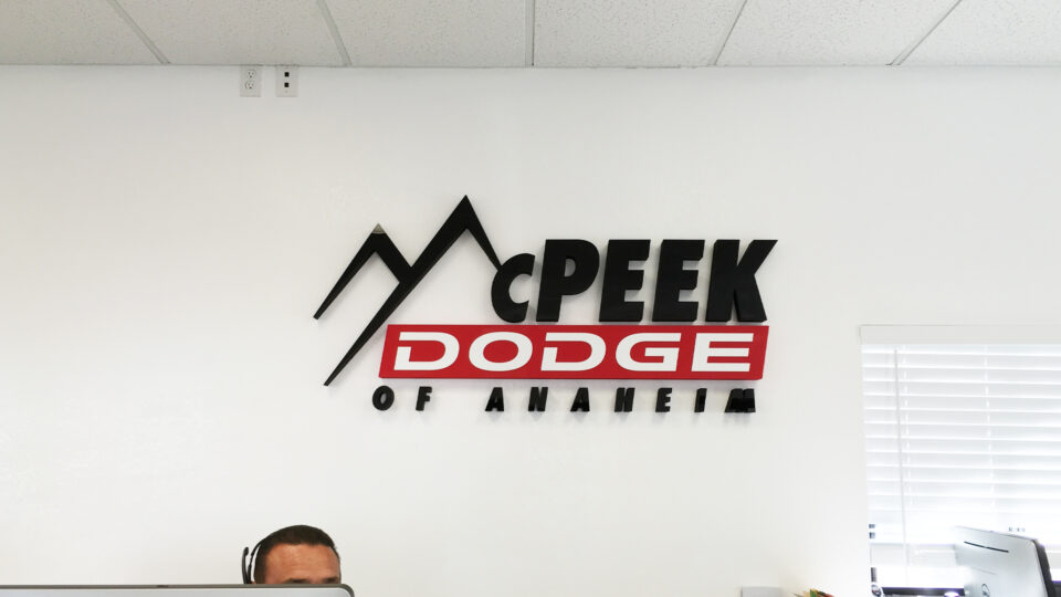 Red, black and white router cut sign on white wall that says McPeek Dodge of Anaheim