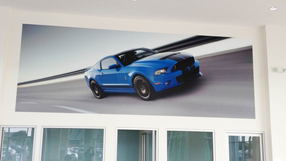 Blue ford mustange on road wall graphic at auto dealer