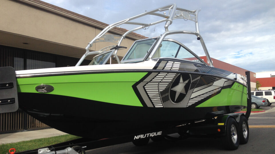 Green, black, gray and white star Nautique boat vinyl wrap, sitting on trailer in parking lot.