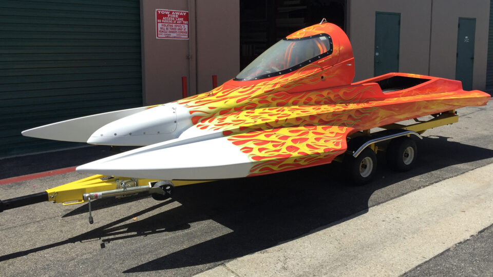 White race boat wrap with orange and yellow flame graphics, sitting on trailer in parking lot