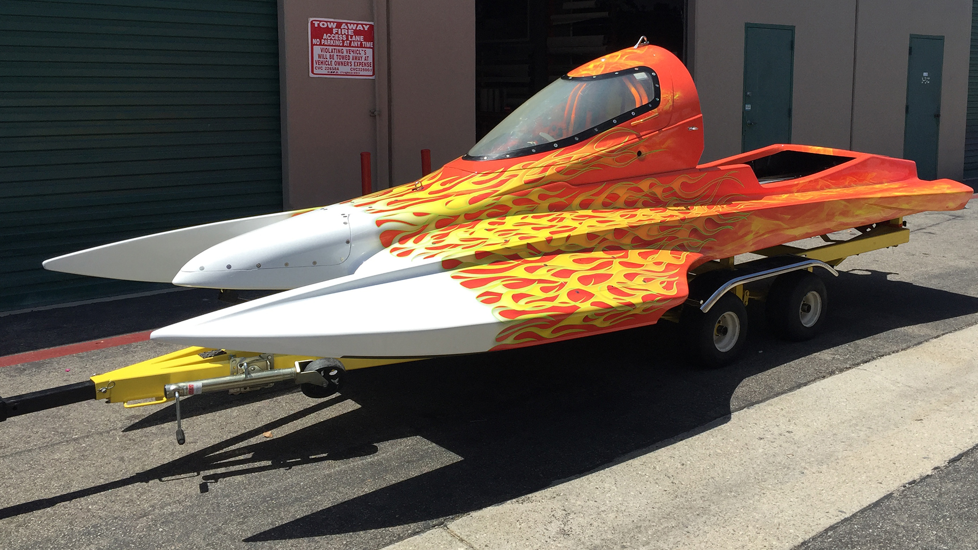 White race boat wrap with orange and yellow flame graphics, sitting on trailer in parking lot