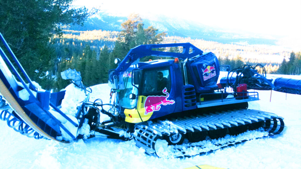 Snow groomer vinyl wrap that says RED BULL with logos in blue, red and yellow, parked in snow at ski resort