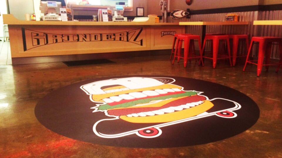 Black round restaurant floor decal with hamburger wearing ballcap on a skateboard
