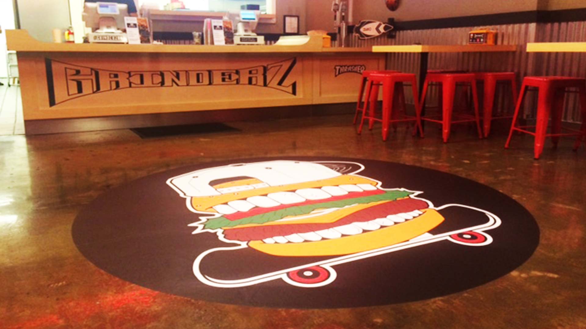 Black round restaurant floor decal with hamburger wearing ballcap on a skateboard