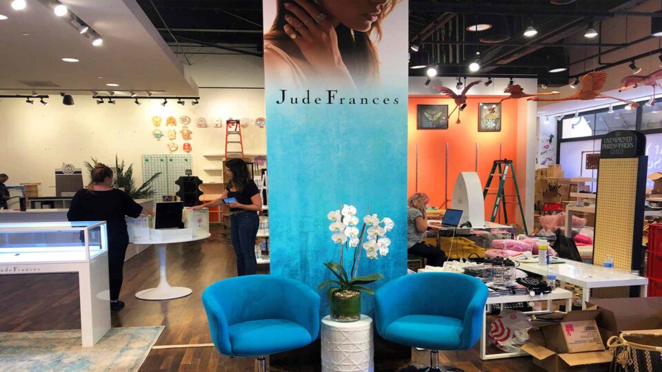 Blue banner with model wearing jewelry inside store with blue chairs and table with orchid