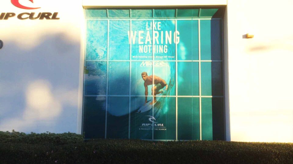 Surfer on wave perforated window graphics with Rip Curl logo and "like wearing nothing"text