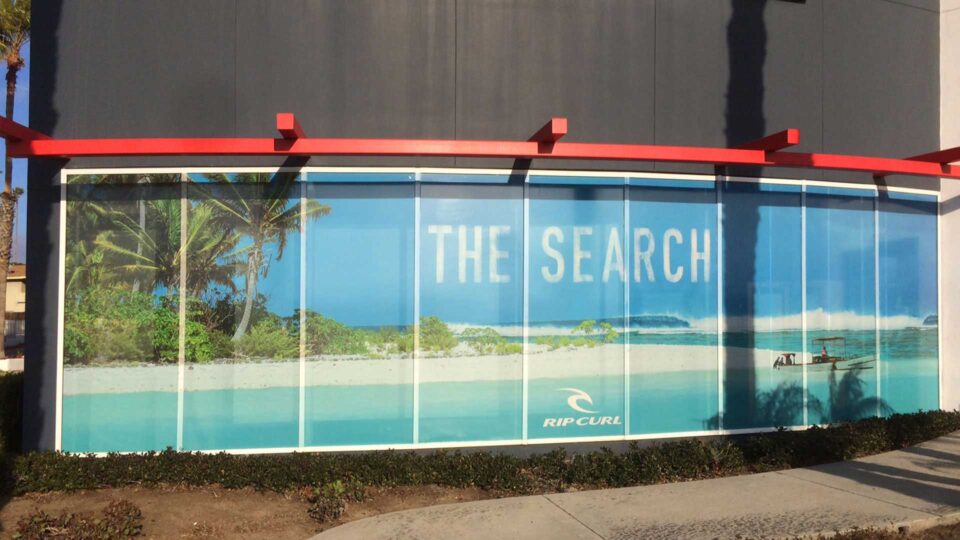 Perforated window graphics of tropical beach with boat and "The Search" with Rip Curl logo