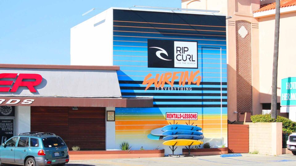 Blue, yellow and orange striped concrete wall mural with Rip Curl logo and Surfing is everything text