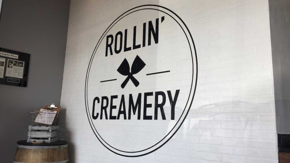 Black die cut decal circle logo for Rollin Creamery on white brick wall