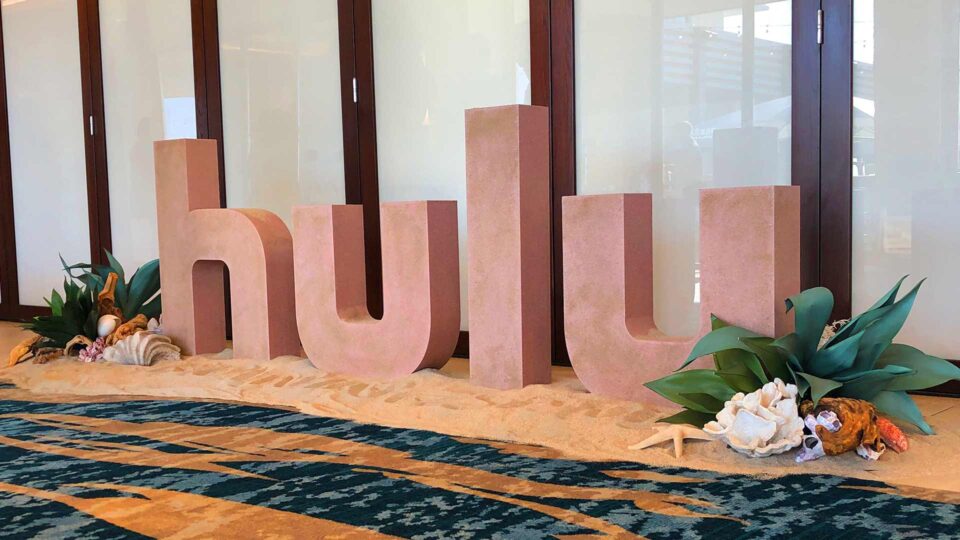 Large sand colored HULU router cut letters on sand with shells and sea plants for sales meeting event