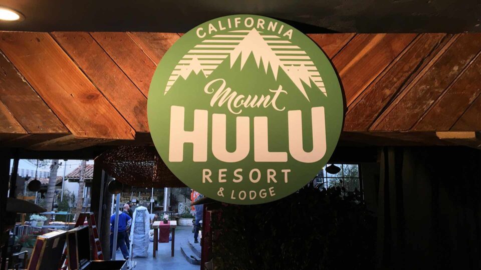 Round green router cut sign with Mount Hulu Resort in white on wood celing in restaurant for sales meeting event.