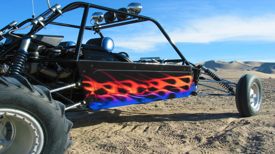 Black sandrail with yellow, red and blue flames on side, parked in the desert