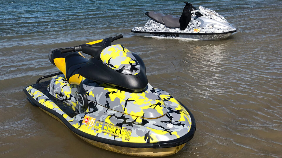 one yellow camoflauge and white camoflauge Seadoo vinyl wraps, sitting in lake.