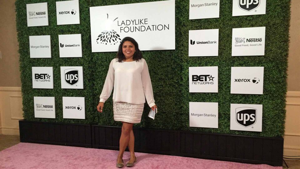 Greenery media wall with white and black event sponsors for Ladylike Foundation. Woman posing in front.