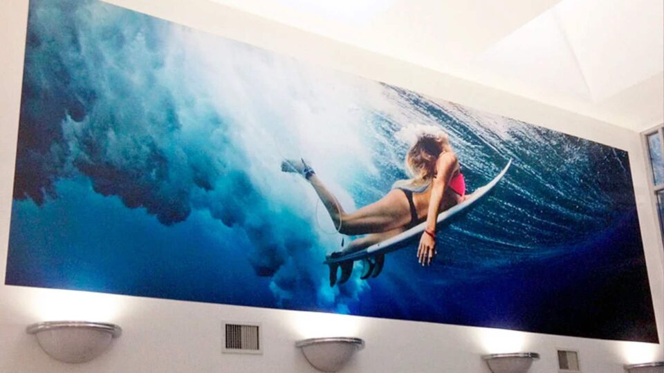 Girl in bikini diving under wave on surfboard wall mural