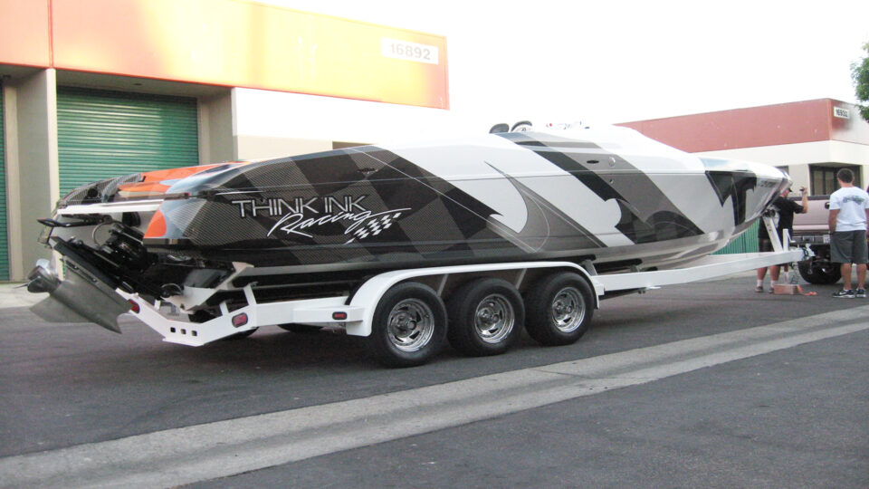 White, black and gray Think Ink racing boat wrap, sitting on trailer in parking lot.