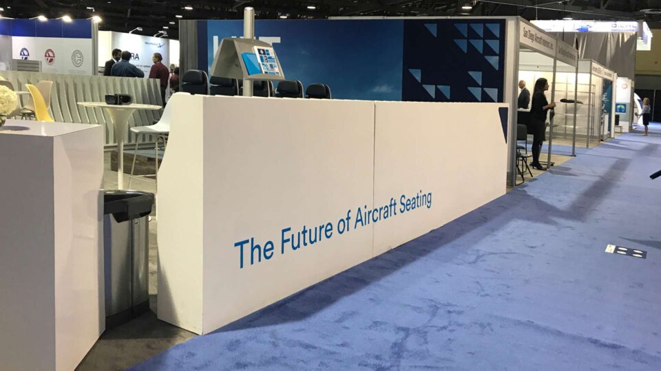 White trade show booth wall with blue "future of aircraft seating" in blue