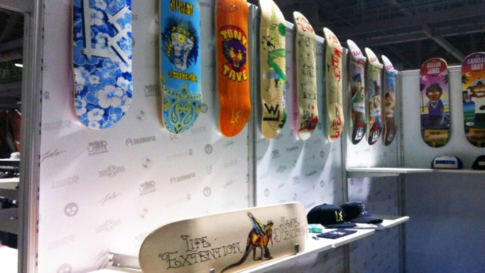 White modular trade show booth walls with white vinyl and sk8Mafia and skateboard brand logos in gray. Colorful skateboards displayed over.