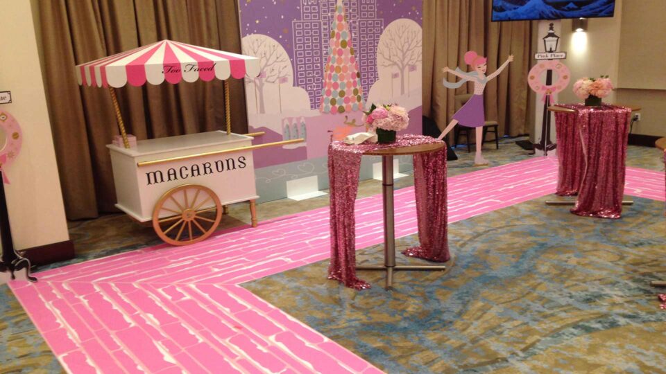 Pink vinyl floor graphic with macaron cart, gator board backdrops and tables with flowers for Too Faced