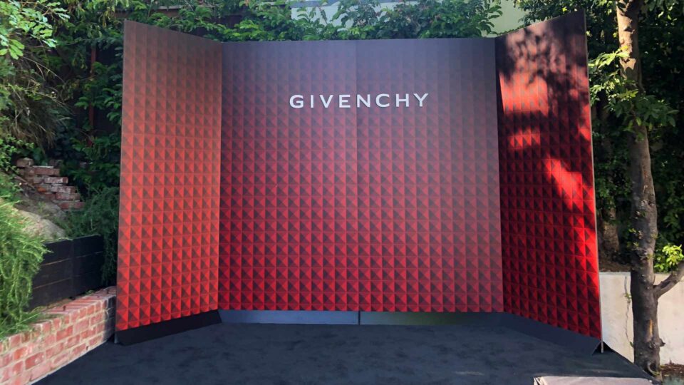 Black and red patterned backdrop wall with white Givenchy text outsdie with greenery behind for event