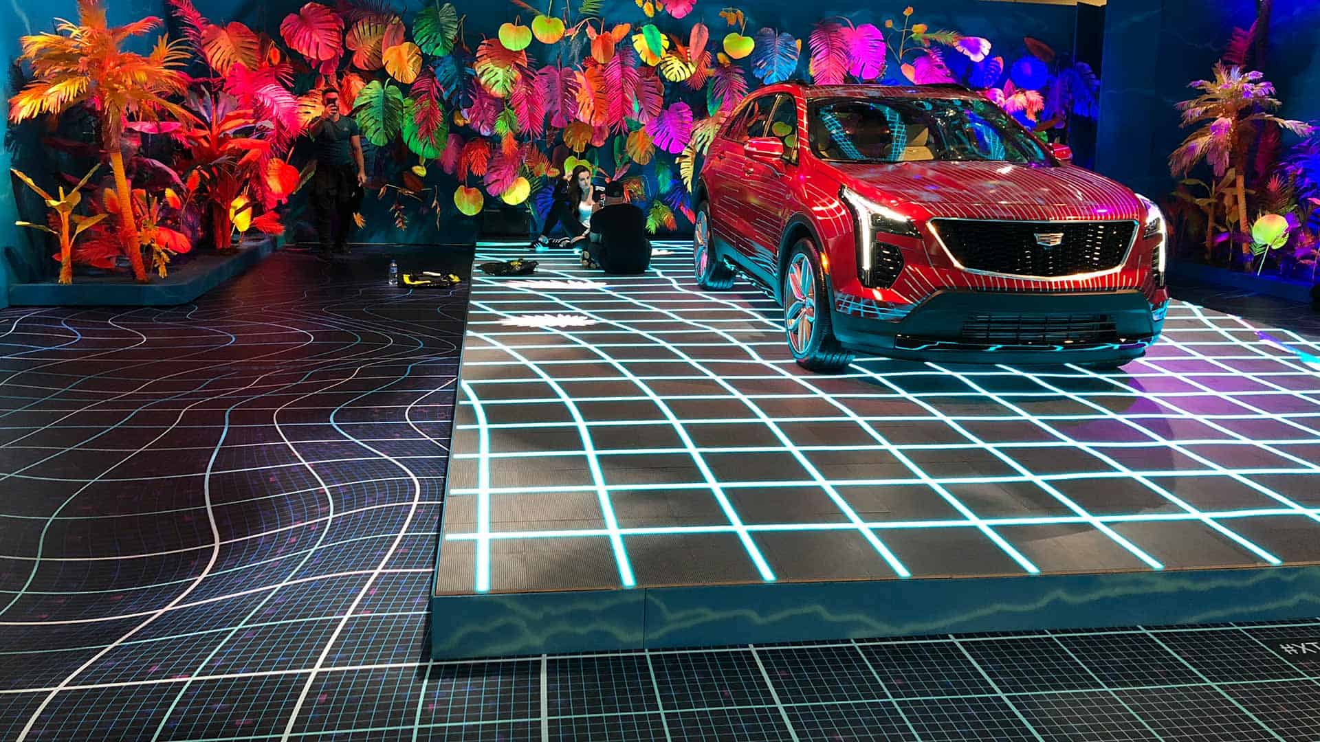 Black and blue grid pattern floor graphic with red Cadillac vehicle on top of it