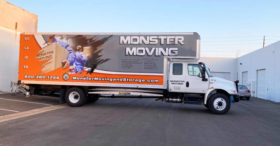 Moving truck with trailer vehicle wrap in gray, white and orange. Features men in blue uniforms moving boxes. White text of logo and services