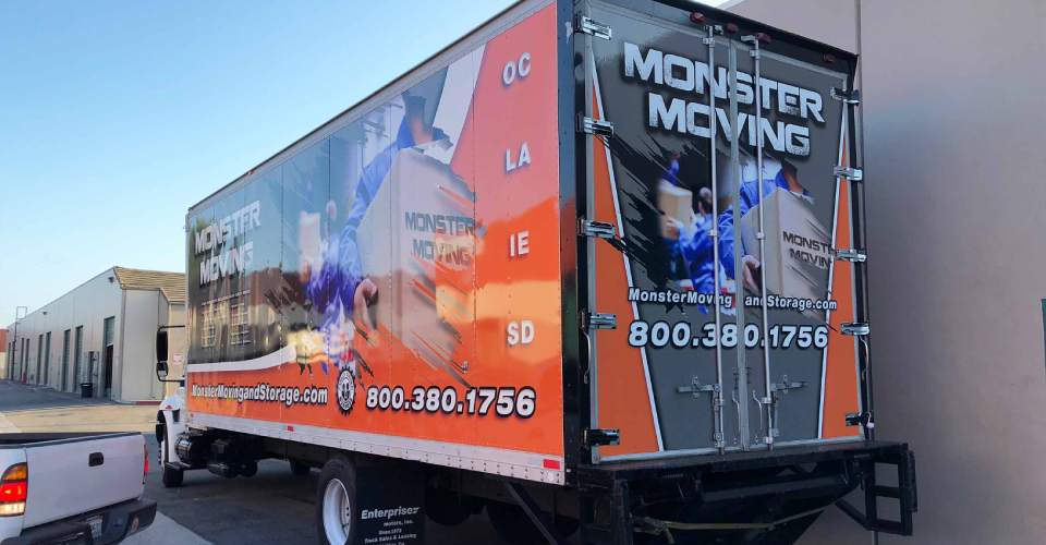 Rear and side view of trailer wrap with gray, white and orane and men in uniforms moving boxes.