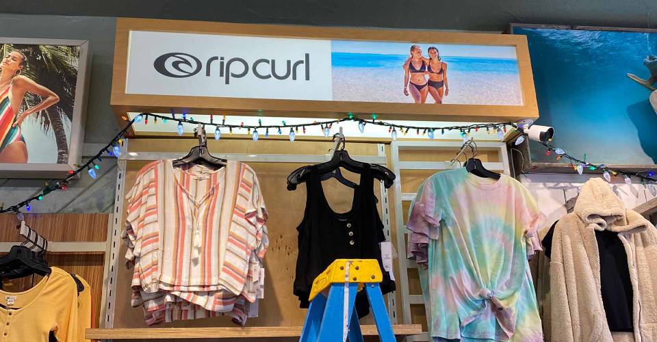 Rip Curl Lightbox above clothes in retail store showing 2 girls in bikinis on the beach and Rip Curl logo