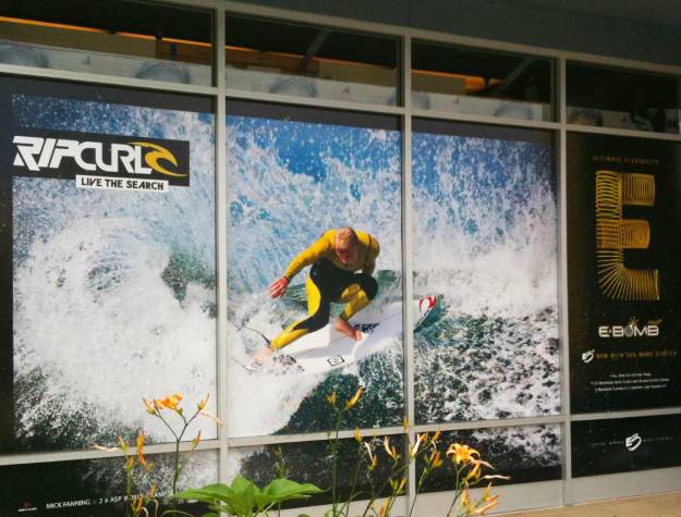 Perforated window of surfer in wetsuit on wave and black and gold Ebomb wetsuit logo